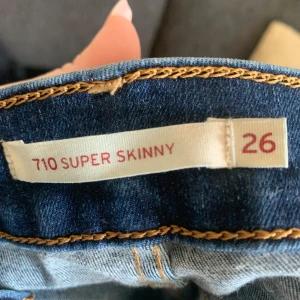 Levi's 710 Super Skinny Jeans - Säljer ett par snygga Levi's 710 Super Skinny jeans i klassisk blå denim. De är i storlek 26 och har den ikoniska Levi's-lappen baktill. Perfekta för en casual look och passar till det mesta i garderoben. Superbekväma och stilrena!