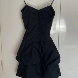 Svart klänning med voluminös kjol - Säljer en superfin svart klänning med smala axelband och en voluminös kjol. Den har en åtsittande överdel med rynkdetaljer och volanger nertill