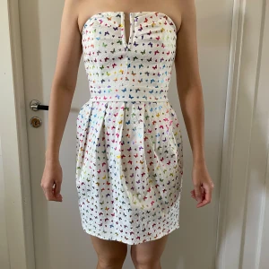 Vit axelbandslös klänning med fjärilsmönster från Goddess London - Säljer en vacker vit axelbandslös cocktailklänning från Goddess London. Den har ett färgglatt fjärilsmönster.  Inga hål eller fläckar. Storlek saknas, uppskattas till S/36