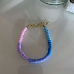 Färgglatt armband med guld detaljer - Säljer ett superfint armband med färgglada pärlor i rosa, lila och blått. Armbandet har justerbara guld kedjor som gör det enkelt att anpassa storleken. Perfekt för att liva upp vilken outfit som helst!