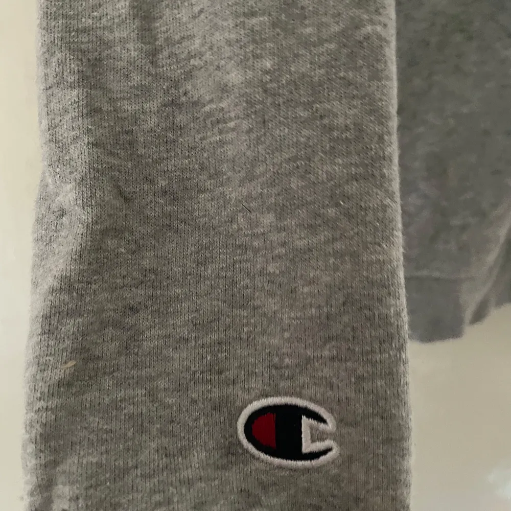 Säljer en grå hoodie från Champion. Den har en klassisk design med Champion-loggan på bröstet och en liten logga på ärmen. Tyvärr finns det några hål på baksidan, men den är fortfarande superbekväm och perfekt för chill dagar. Passar bra till både jeans och mjukisbyxor!. Tröjor & Koftor.