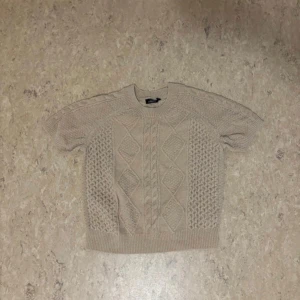 Beige stickad tröja - Säljer en superfin beige stickad tröja med snyggt mönster. Den har korta ärmar och ribbade kanter som ger en skön passform. Perfekt för höst och vår när det är lite kyligt ute. Passar både till jeans och kjol!