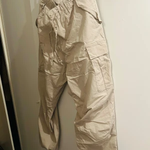 Beige cargobyxor från H&M - Säljer ett par beige cargobyxor från H&M i storlek L. Byxorna har en regular fit och är perfekta för en avslappnad stil. De har flera praktiska fickor på sidorna och en bekväm midja med snörning. Perfekta för vardagsbruk eller en casual utflykt!
