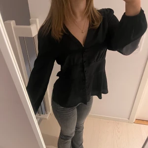 Svart blus med knappar - Snygg svart blus med knappar framtill och långa ärmar. Är i strlk 40 men jag är vanligtvis xs. Beroende på hur tight eller pösigt man vill ha den! Knapparna går att knäppa upp! 