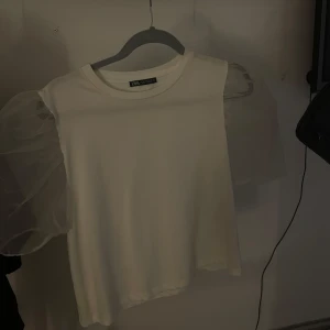 Vit topp med puffärmar från Zara - Säljer en stilren vit topp från Zara med unika puffärmar i ett transparent material. Toppen har en rund halsringning och är perfekt för att ge en elegant touch till din outfit.