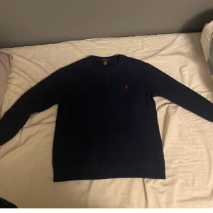 Mörkblå tröja från Polo Ralph Lauren - Säljer en stilren mörkblå tröja från Polo Ralph Lauren med det klassiska röda logotypbroderiet på bröstet. Tröjan har långa ärmar och en rund halsringning. Perfekt för en avslappnad och snygg look.