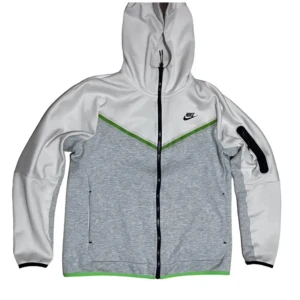 Grå och vit huvtröja från Nike - Säljer en snygg grå och vit huvtröja från Nike med dragkedja och huva. Tröjan har svarta detaljer och en grön linje som ger en sportig look. Perfekt för en casual stil.