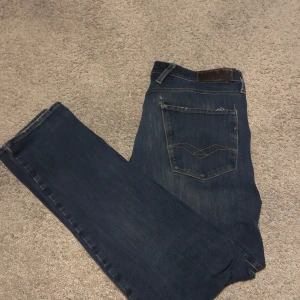 Säljer ett par feta Replay jeans bjuder på bältet. W33-L32 - Snygga mörkblå jeans med subtila slitningar för en trendig look. Jeansen kommer med ett matchande bälte i mörkblått, perfekt för att komplettera din stil.