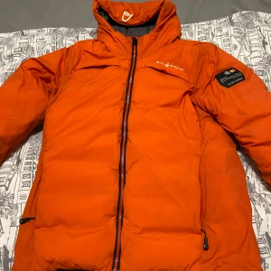 Orange dunjacka från Sail Racing - Säljer en cool orange dunjacka från Sail Racing. Jackan har en dragkedja framtill och är långärmad. Perfekt för kalla dagar med sin varma och skyddande design. Den har en stilren look med märkets logga på bröstet och en patch på ärmen.