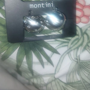 Silverfärgade örhängen från Montini - Snygga silverfärgade örhängen från Montini med glittrande stenar. Perfekta för att ge en elegant touch till din outfit. Kommer i originalförpackning från Ur & Penn.