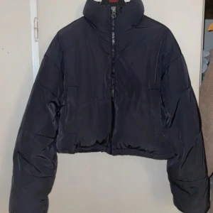 Svart pufferjacka  - Säljer en svart pufferjacka  med dragkedja framtill. Jackan har en hög krage och är croppad i modellen. Perfekt för kyligare dagar.