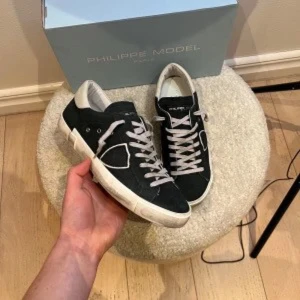 Svarta sneakers från Philippe Model - Snygga svarta sneakers från Philippe Model med vita detaljer och snörning. Skorna har en vit sula och en stilren design som passar perfekt till vardags. De är tillverkade i skinn och har en bekväm passform.