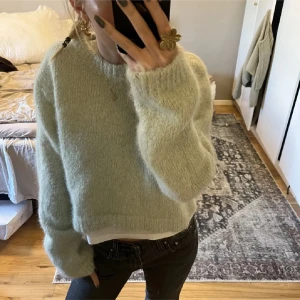 Ljusgrön stickad tröja - Mysig ljusgrön stickad tröja med en croppad passform. Tröjan har långa ärmar och en rund halsringning, perfekt för kyligare dagar. Den fluffiga texturen ger en extra touch av komfort och stil.