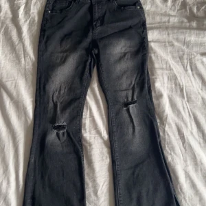 Svarta bootcut jeans med slitningar - Snygga svarta bootcut jeans med slitningar på knäna. Och slitsar längst ner på vaden högmidjade. Använda ett par gånger och är i bra skick. Nytvättade och rollade. Från början på byxan till slut är den 102 cm. Den är liten i storlek skulle säja M 