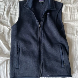 Mörkblå fleeceväst från Patagonia - Säljer en mörkblå fleeceväst från Patagonia med dragkedja framtill. Västen har en hög krage och två fickor med dragkedja. Perfekt för kyliga dagar.