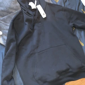 Svart hoodie från Adidas - Säljer en svart hoodie från Adidas med texten 'ALL SZN' broderad på ärmen. Tröjan har en klassisk känguruficka och justerbar huva med dragsko. Perfekt för en avslappnad stil.