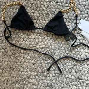 Svart bikiniöverdel med kedjedetaljer -  svart bikiniöverdel med guldfärgade kedjor som axelband. 