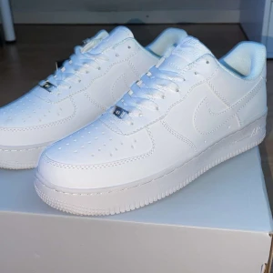 Vita Nike Air Force 1 - Snygga och klassiska vita Nike Air Force 1 med snörning. Perfekta för en stilren look. Skorna har en robust sula och är tillverkade i syntetmaterial.stolek 44-45 