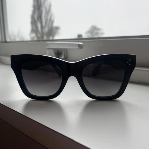 Svarta solglasögon från Celine - Snygga svarta solglasögon från Celine med en elegant cat-eye design. De har en tjock båge och små dekorativa nitar på framsidan. Perfekta för att ge en stilren look. Nästan helt oanvänd. Orginapris på runt 4500kr 