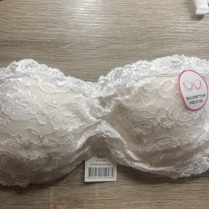 Vit spets balconette-BH - Säljer en elegant vit balconette-BH från Body Secrets. Den är täckt med vacker spets och har en liten rosett framtill. BH:n har bygel för extra stöd och justerbara band för perfekt passform.