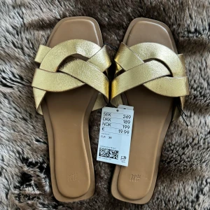 Guldiga tofflor från H&M - Snygga guldiga tofflor från H&M med flätad design. (Skulle säga att de är som en 38)