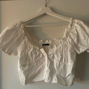 Vit blus från Gina Tricot - Charmig vit blus från Gina Tricot med korta puffärmar och elastisk smockdetalj vid hals och ärmslut. Perfekt för en somrig look 🌸🍓