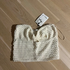 Vit tubtopp från Pull&Bear - Säljer en snygg vit tubtopp från Pull&Bear med en unik textur. Perfekt för att skapa en stilren look. Toppen är i storlek S och har en bekväm passform. Den är ganska liten i storleken men sitter väldigt fint