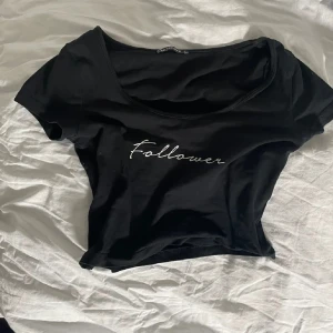 Svart croppad t-shirt med text - Snygg svart croppad t-shirt med texten 'Follower' i vitt. Perfekt för en avslappnad stil. Kortärmad och i mjukt material.