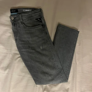 Grå jeans från Replay - Snygga grå jeans från Replay med slitningar. Modell Rocco, storlek W:31 L:34. Jeansen är uppsydda ungefär 8 cm. Jag är 192 lång och dom sitter bra på mig.
