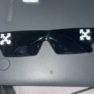 Svarta solglasögon med märket off white - Snygga svarta solglasögon med en rektangulär form och vit logotyp på sidorna från off white Perfekta för en stilren look.