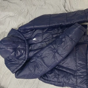 Mörkblå dunjacka från Ralph Lauren - Säljer en snygg mörkblå dunjacka från Ralph Lauren OBS! Inte äkta med huva och dragkedja. Jackan har ett quiltat mönster och den ikoniska loggan på bröstet. Perfekt för kyliga dagar! 