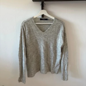 Grå stickad tröja från Vero Moda - Säljer en stilren grå stickad tröja från Vero Moda. Tröjan har en v-ringad hals och långa ärmar, perfekt för kyligare dagar. Den är mjuk och bekväm, idealisk för både vardag och avslappnade tillfällen. Passar bra till jeans eller kjol.