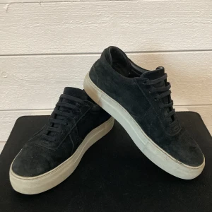 Axel Arigatos skor - Snygga svarta sneakers i mocka med vit sula och klassisk snörning. Perfekta för en stilren look. Inga synliga skador bara lite smuts som jag inte lyckas få bort hör av er till oss för mer info