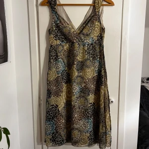 Sommarklänning med blommor - Säljer en unik klänning med ett färgglatt blommönster i beige, blått och brunt. Klänningen har en v-ringad design och knytband i midjan för en justerbar passform. En äldre HM modell som jag köpt på loppis, perfekt för sommaren!!🌸