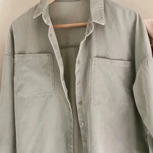 Grön overshirt från Pimkie - Snygg grön overshirt från Pimkie med två stora bröstfickor och knappar framtill. Perfekt för lager-på-lager stil. Skjortan har en klassisk krage och är tillverkad i ett mjukt material.