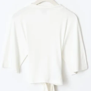 Vit croppad topp med knytband  - Säljer en stilren vit croppad topp med knytband i midjan. Toppen har korta ärmar och en öppen rygg som ger en trendig look. Perfekt för varma dagar eller sommarens fester.