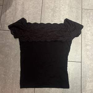 Snygg svart offshoulder topp med spetsdetaljer på överdelen. Perfekt för en stilren look. Toppen har en tight passform och är tillverkad i ett mjukt material.