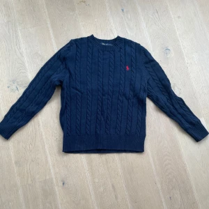 Mörkblå kabellstickad  tröja från Ralph Lauren - Säljer en stilren mörkblå stickad tröja från Ralph Lauren.  Helt nytt skick . Tveka ej att ställa någon fråga !