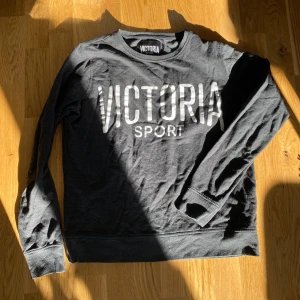 Svart/Grå långärmad tröja från Victoria Sport - Svart/Grå melerad långärmad tröja från Victoria Sport med tryck framtill. Mjuk och bekväm. Storlek M för en lite lösare fit men passar nog S för oversized. 