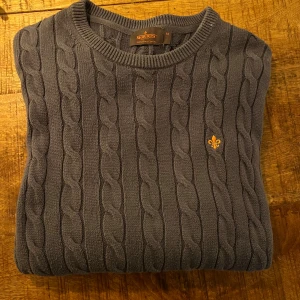 Kabelstickad tröja från Morris - Säljer en stilren grå kabelstickad tröja från Morris. Tröjan har en broderad detalj på bröstet och ribbad krage. Perfekt för kyligare dag ellr på sommaren. Tröjan har en liten fläck på kragen men tror det går bort i tvätten. Nypris 1700. Hör av er om ni har några frågor