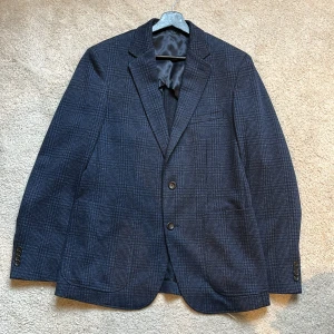 Mörkblå rutig kavaj från Mango Man - Snygg mörkblå kavaj från Mango Man i slim fit. Kavajen har ett diskret rutmönster och stängs med två knappar framtill. Perfekt för en stilren look.