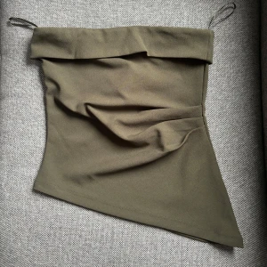 Grön tubtopp från Gina Tricot - Helt ny - Snygg mörkgrön tubtopp från Gina Trigot i en stilren design. Toppen har en asymmetrisk nederkant och är perfekt för en trendig look. Tillverkad i ett mjukt och bekvämt material. Helt oanvänd med prislapp kvar!!!!💓