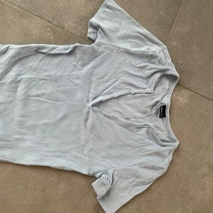 Ljusblå ribbad topp från Gina Tricot - Säljer en ljusblå ribbad topp från Gina Tricot. Toppen har korta ärmar och knappar framtill som ger en snygg detalj. Perfekt för en avslappnad stil.