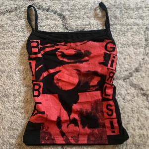 Svart och röd linne med tryck - Snygg svart linne med rött tryck och text. Linnet har smala axelband och en liten rosett framtill. Använd gärna köp nu <3