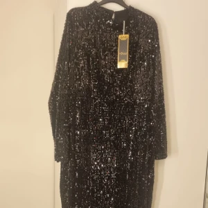 Svart glittrig klänning  - Snygg svart långklänning täckt med glittriga paljetter. Perfekt för en glamorös kväll. Klänningen har långa ärmar och en elegant passform som ger en sofistikerad look.