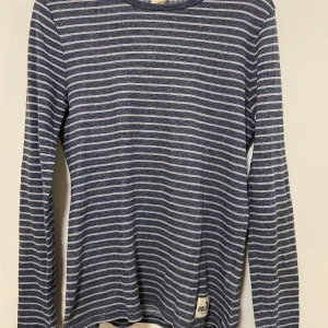 Blå och vit randig tröja från Hollister - Säljer en snygg blå och vit randig tröja från Hollister. Tröjan har långa ärmar och en bekväm passform. Perfekt för en avslappnad stil. Hollister-loggan syns på framsidan. Sparsamt använd, så fint skick. Passar både strl S/M