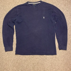 Blå långärmad tröja från Polo Ralph Lauren - Säljer en stilren blå långärmad tröja från Polo Ralph Lauren. Tröjan är tillverkad i 100% bomull och har en diskret logga på bröstet. Perfekt för en avslappnad och snygg look.