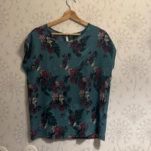 Blommig topp i blått och rött - Snygg blommig topp i blått med röda och vita blommor. Toppen har en rund halsringning och korta ärmar. Perfekt för en somrig look!