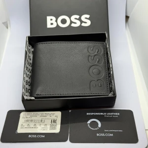 BOSS Black Leather Style Big BB_6 cc  - BOSS Black Leather Style Big BB_6 cc   A signature billfold wallet by BOSS in grained leather with a large embossed logo on the front.   Length: 11,0 cm Width: 1,5 cm Height: 8,0 cm  2 inside open pockets 2 bill compartments 6 credit card slots  Fully lined Embossed logo  Packaging: Box