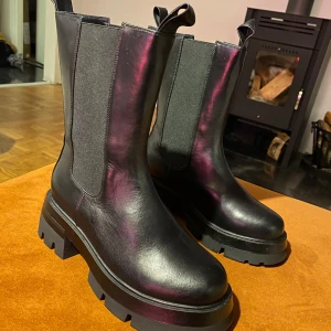 Svarta boots med grov sula - Snygga svarta boots i skinn med grov sula och elastiska paneler på sidorna för enkel på- och avtagning. Perfekta för en stilren look med extra komfort. Passar utmärkt till både jeans och kjol.